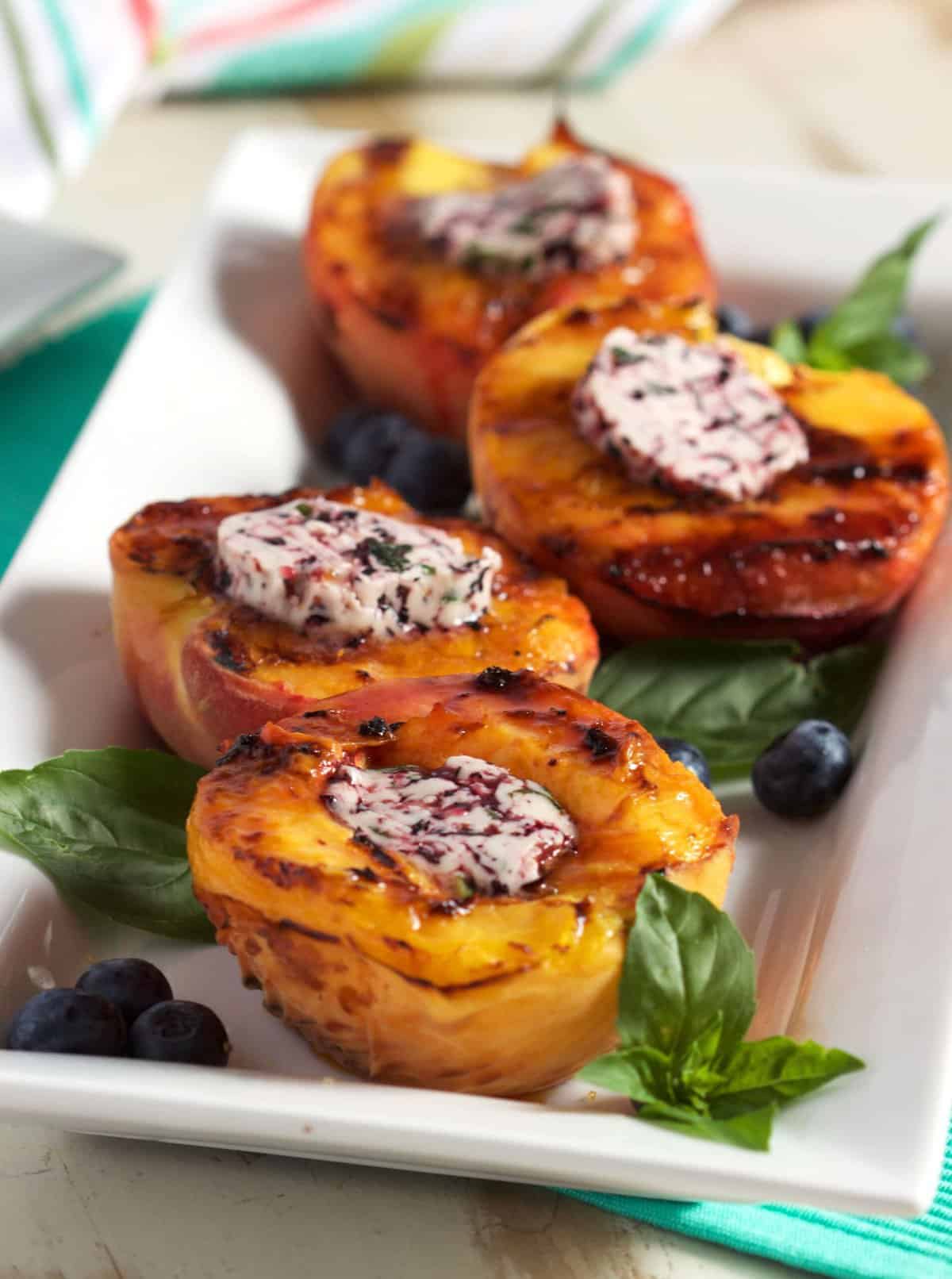 grilled peaches on a platter with basil and blueberries.