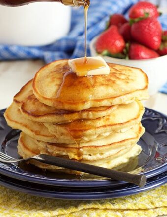 Pile of pancakes on a blue plate with a bowl of strawberries in the background.