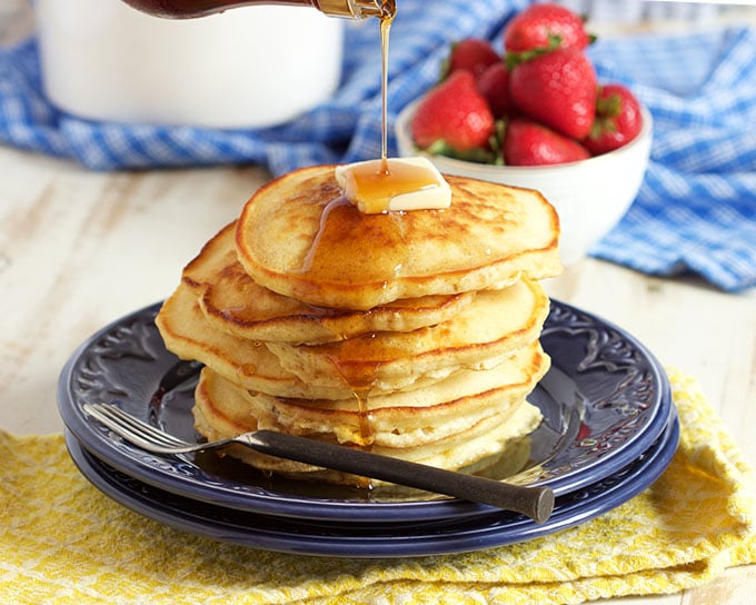 Pile of pancakes on a blue plate with a bowl of strawberries in the background.