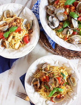 two white bowls with linguine and clams with a serving bowl to the right.