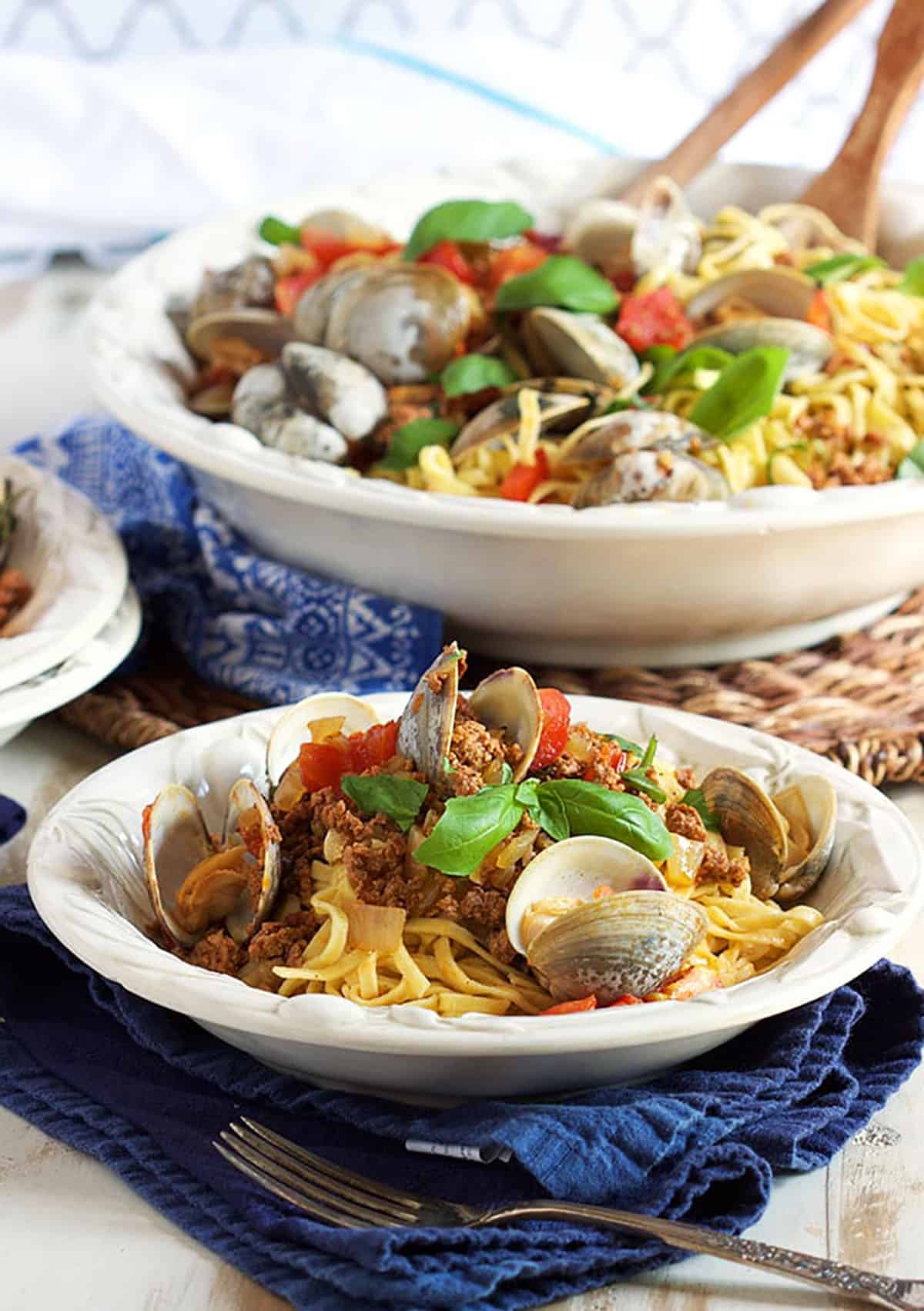 white bowl with linguine topped with clams and chorizo with a serving bowl in the background.