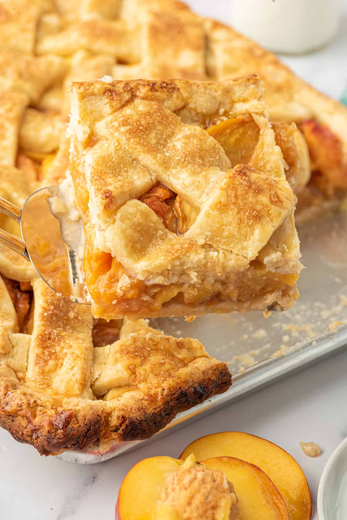 A slice of peach slab pie is being lifted from the pie dish.