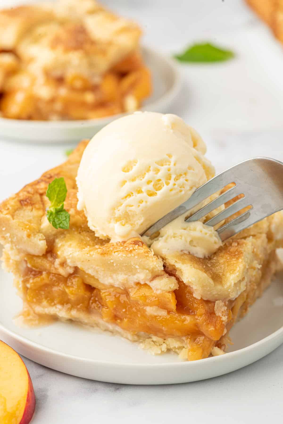 A piece of pie is being eaten with a fork. There's a scoop of vanilla ice cream on top.
