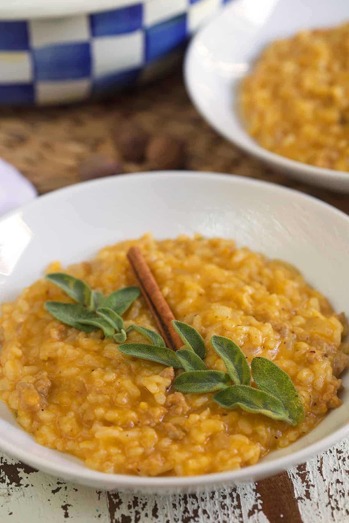 A bowl of risotto is topped with a cinnamon stick and fresh sage.