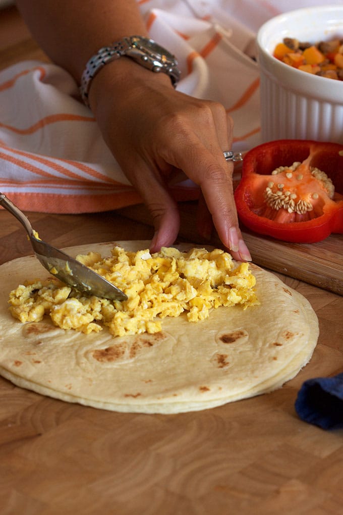 scrambled eggs being spooned onto the center of a tortilla.