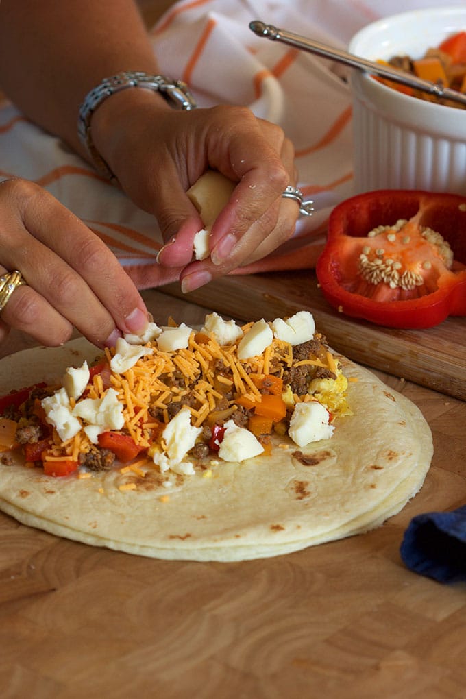 breakfast burrito being assembled with cheese.