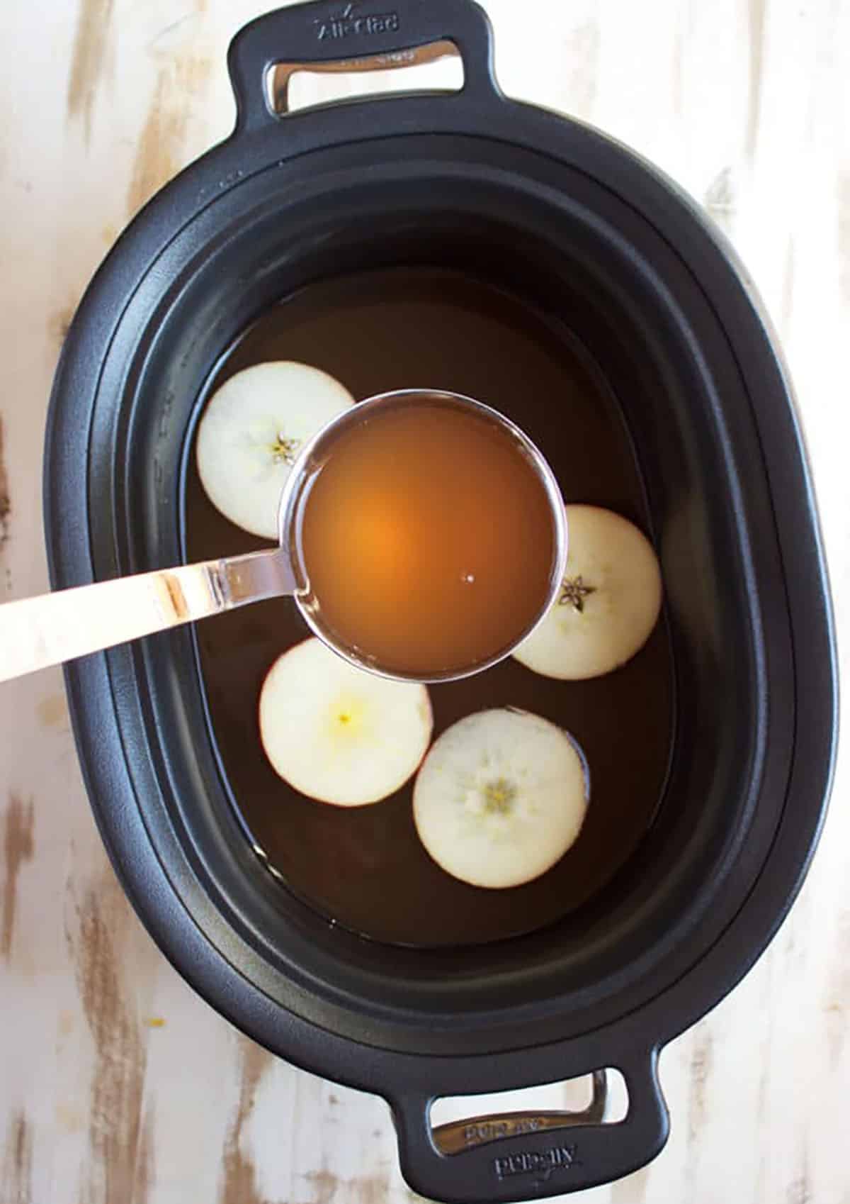 Apple cider in a slow cooker being served with a ladle.