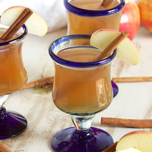Homemade Apple Cider in three footed glasses with cinnamon sticks and apple slice.