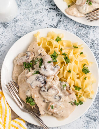 A white plate is topped with chicken marsala and cooked pasta.