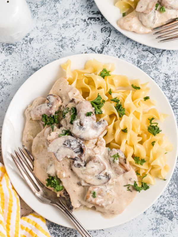 A white plate is topped with chicken marsala and cooked pasta.