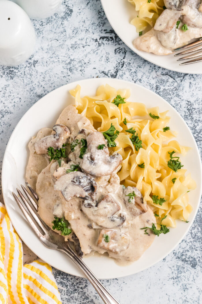 A white plate is topped with chicken marsala and cooked pasta.