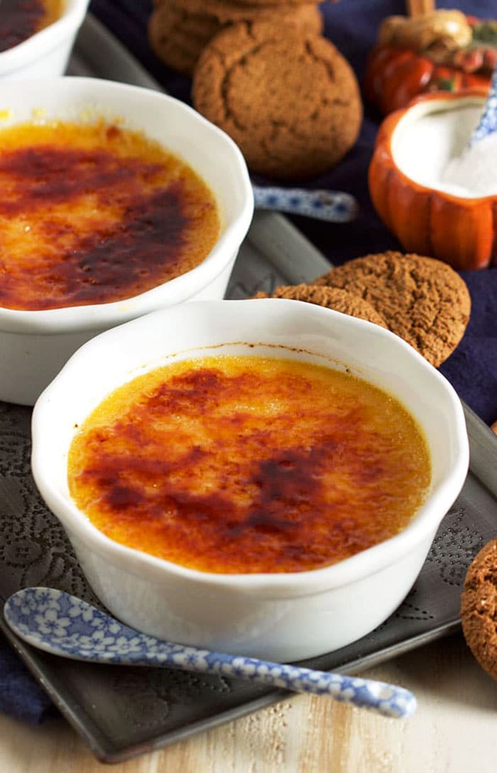 Pumpkin creme brulee in a white ramekin with a blue and white spoon and a pile of gingersnap cookies.