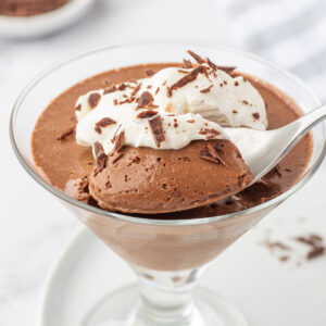 A spoon is digging into a glass of chocolate cream.