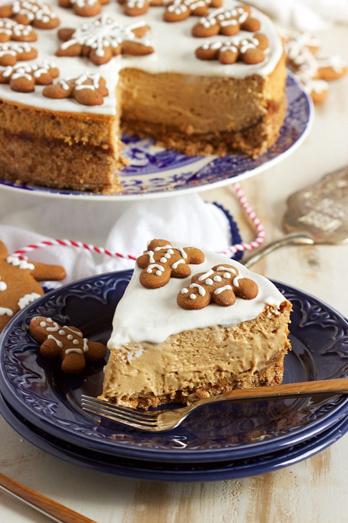 SLICE OF GINGERBREAD CHEESECAKE ON A BLUE PLATE WITH A WHOLE CAKE IN THE BACKGROUND DECORATED WITH GINGERBREAD MEN.