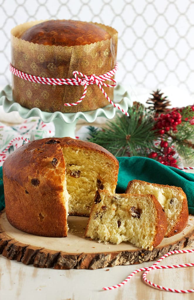 Two loaves of panettone one on a green napkin with a slice taken out and one on a green cake plate with a red and white ribbon tied around. it
