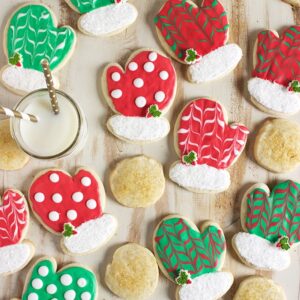 Christmas Sugar Cookies on a wood background, cookies shaped like mittens and decorated with red and green icing.