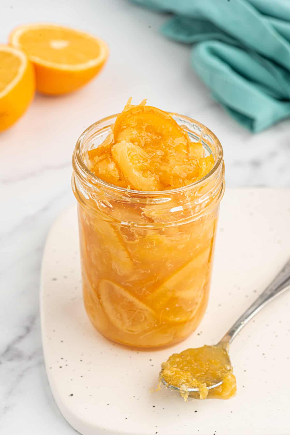 A spoon is sitting next to an open jar of orange marmalade.