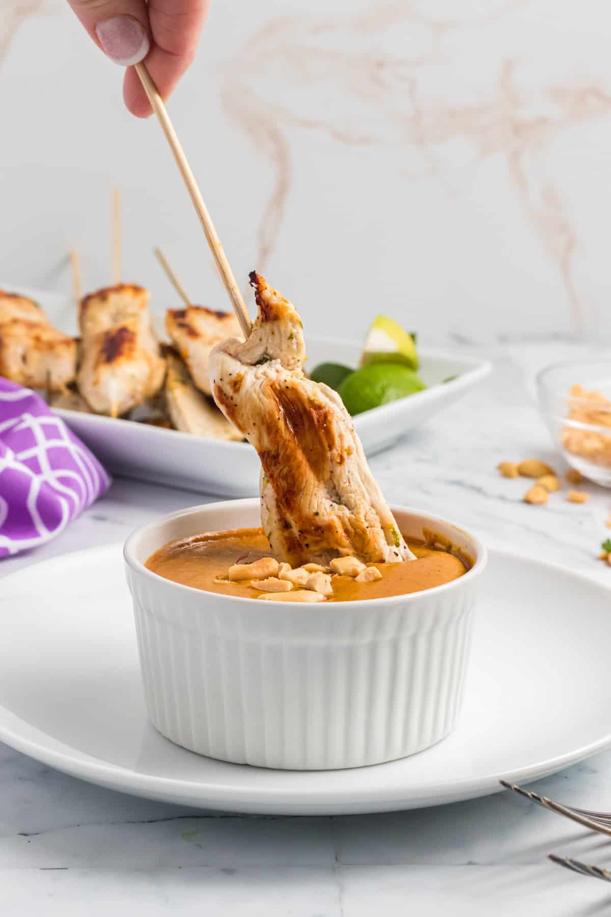 Grilled chicken on a skewer is being dipped into a cup of peanut sauce.