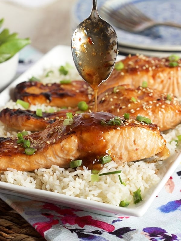 Sweet Chili Orange Glazed Salmon on a bed of rice with sauce being drizzled over top.