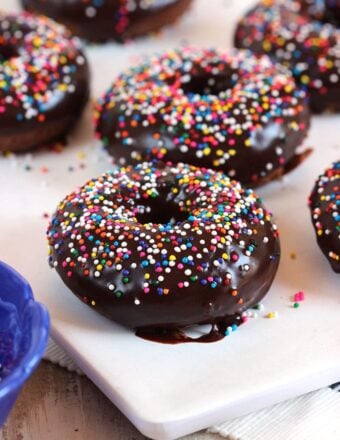Chocolate Glazed donuts on a white board with rainbow sprinkles.