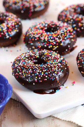 Chocolate Glazed donuts on a white board with rainbow sprinkles.