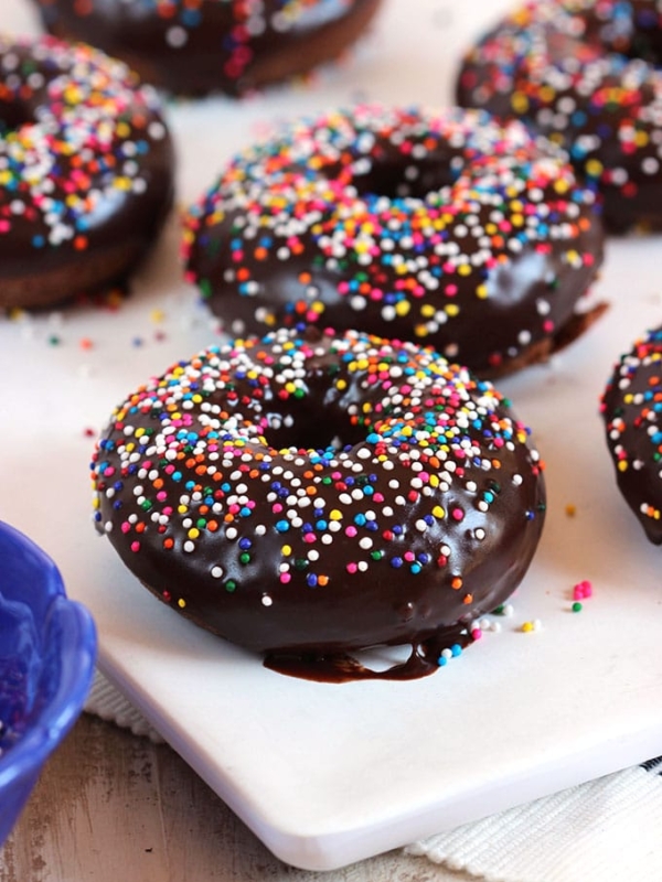 Chocolate Glazed donuts on a white board with rainbow sprinkles.