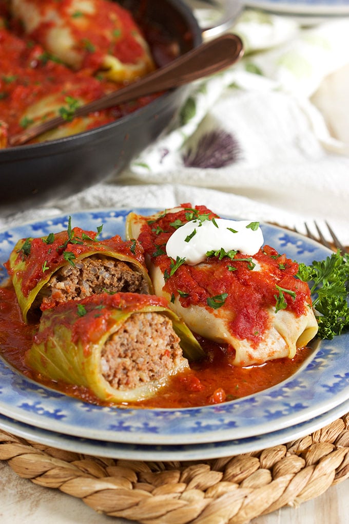 two stuffed cabbage rolls on a blue plate, one cut in half and the other has sour cream on top.