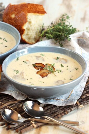Cream of mushroom coup in a gray bowl on a wooden twig placemat with bread in the background.