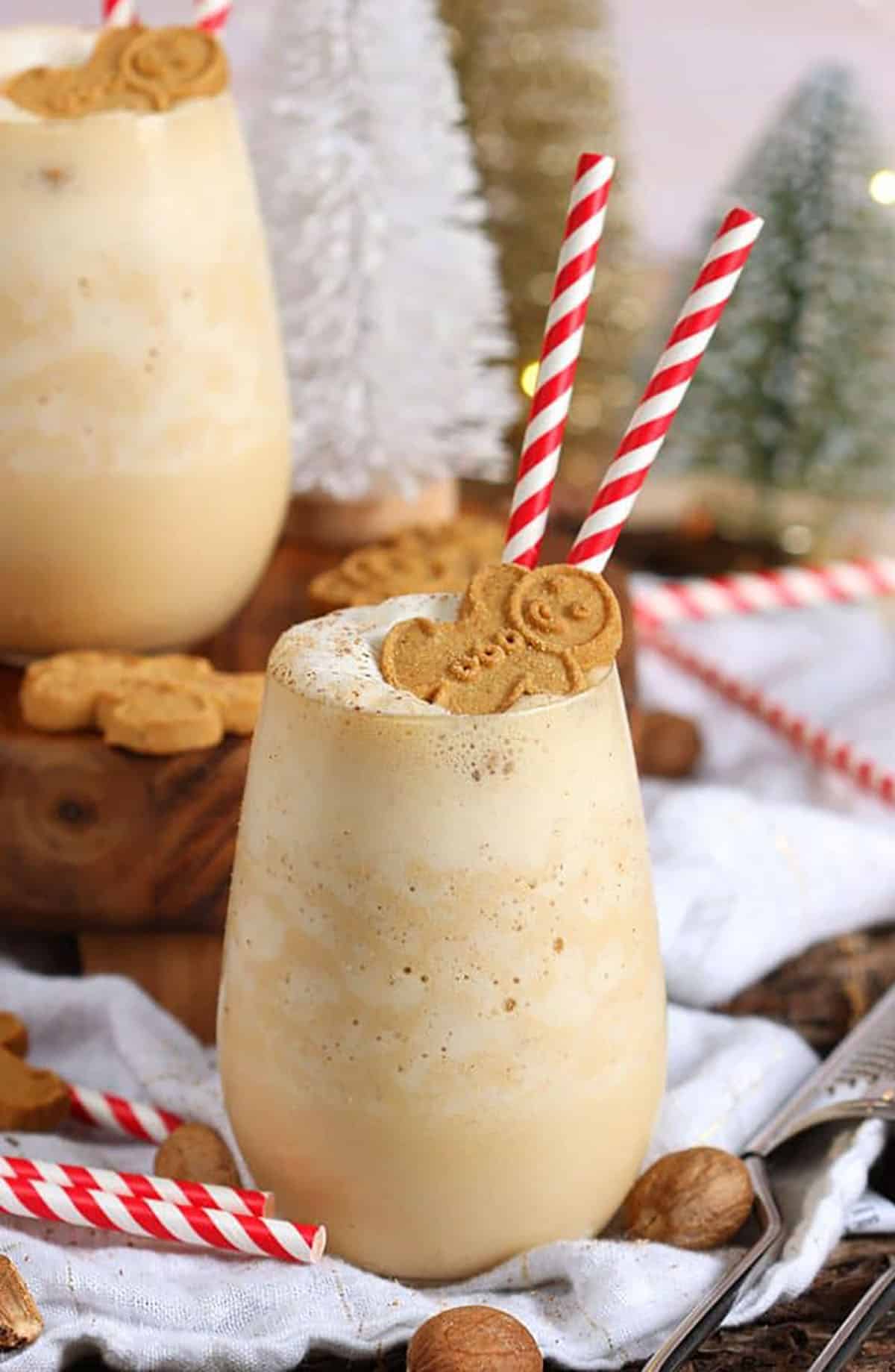 Gingerbread Cheesecake Smoothie in a stemless wine glass with two red and white striped straws and a gingerbread man on top.