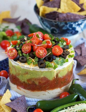 7 layer mexican dip in a glass bowl with chips in the background.