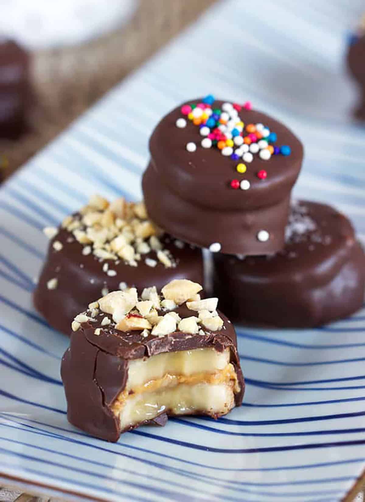 Frozen Chocolate covered banana bites on a blue and white striped plate with a bite out of one of the banana bites.
