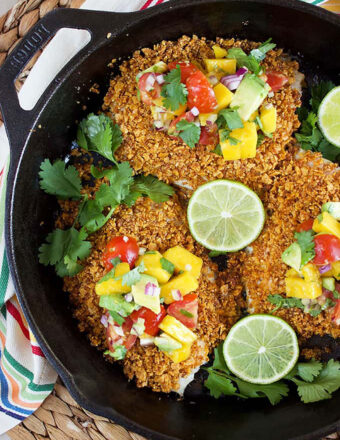 Tortilla Crusted Tilapia in a cast iron skillet with mango salsa on each filet