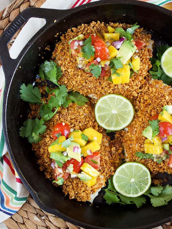 Tortilla Crusted Tilapia in a cast iron skillet with mango salsa on each filet