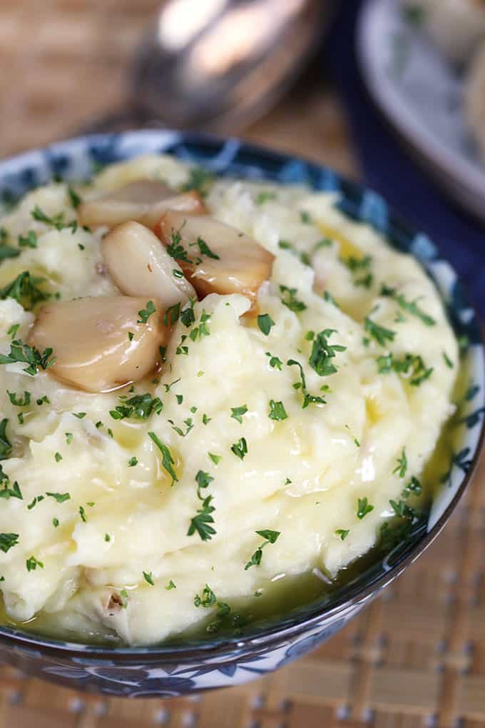 Roasted Garlic Mashed Potatoes with blue and white bowl with roasted garlic cloves on top. TheSuburbanSoapbox.com