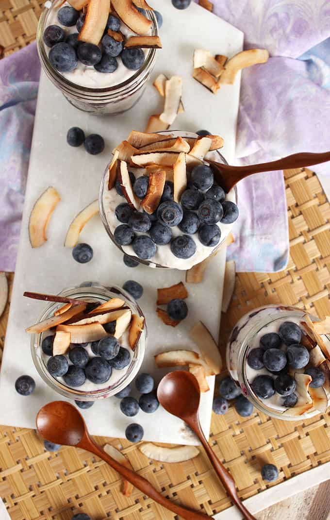 Easy to make toasted coconut overnight oats with blueberries in jars on a marble board. From TheSuburbanSoapbox.com