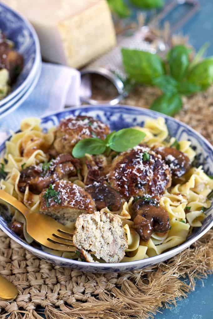 One Pot Chicken Marsala Meatballs recipe over egg noodles with a bite taken from a meatball on a blue and white bowl from TheSuburbansoapbox.com