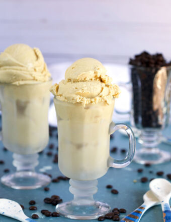 Homemade Coffee Ice Cream in an Irish coffee glass with a glass of coffee beans and white ceramic spoons on a blue background from TheSuburbanSoapbox.com