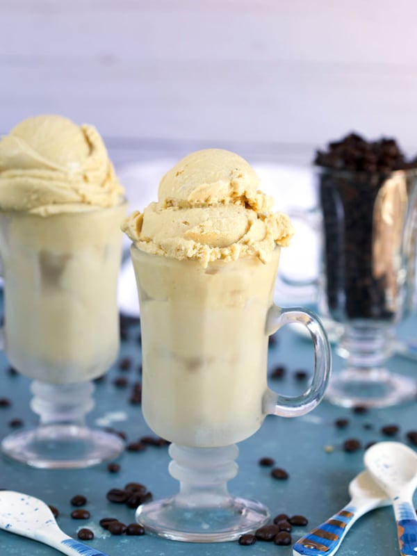 Homemade Coffee Ice Cream in an Irish coffee glass with a glass of coffee beans and white ceramic spoons on a blue background from TheSuburbanSoapbox.com