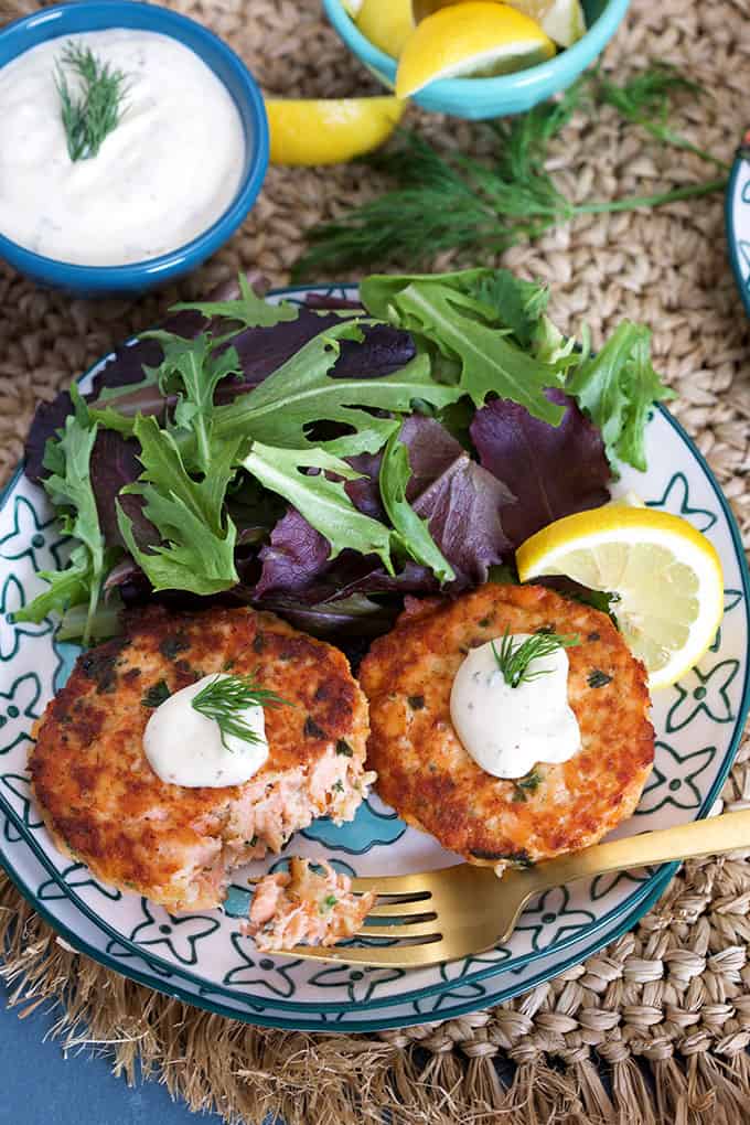 Overhead shot of Salmon Cakes Recipe with Lemon Dill Sauce on a blue and white plate with sauce in a blue bowl