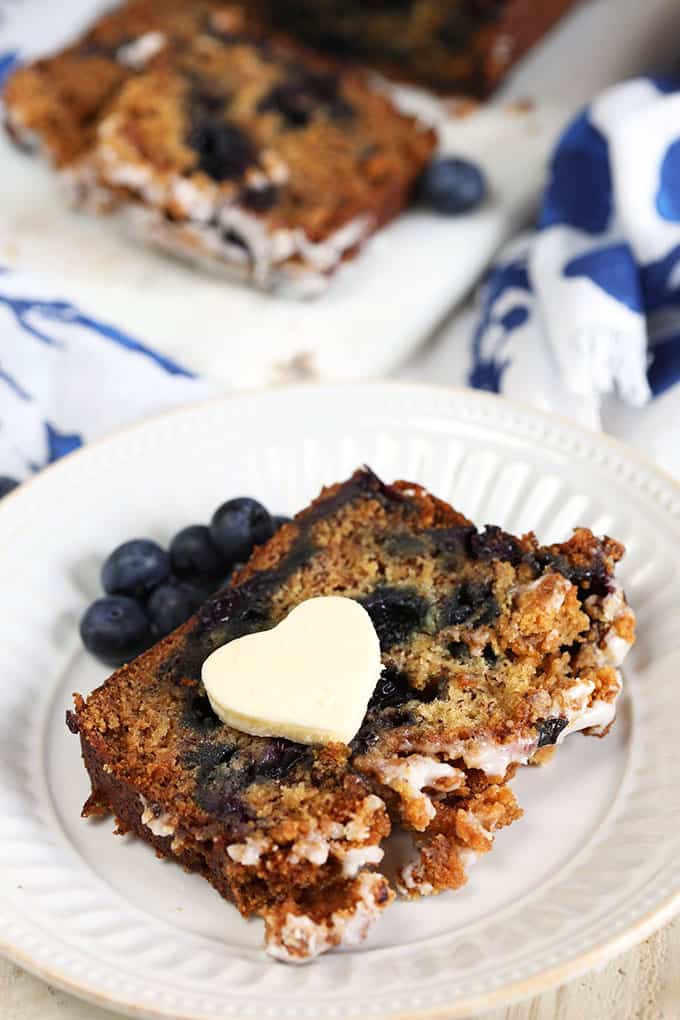 A slice of Blueberry Banana Bread with a heart shaped butter pat on a white plate from TheSuburbanSoapbox.com