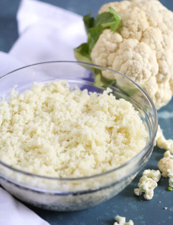 Glass bowl of cauliflower rice on a blue background from Thesuburbansoapbox.com