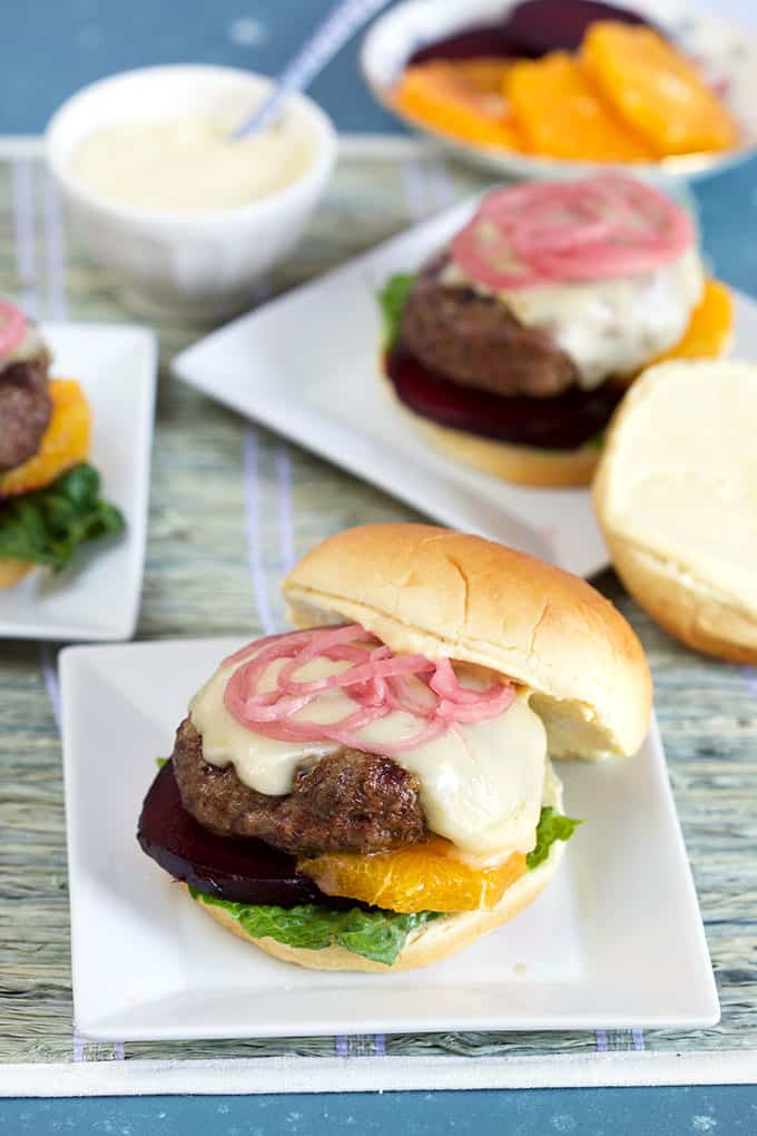 Three lamb burgers with red onions, oranges and beets on a blue background from TheSuburbansoapbox.com