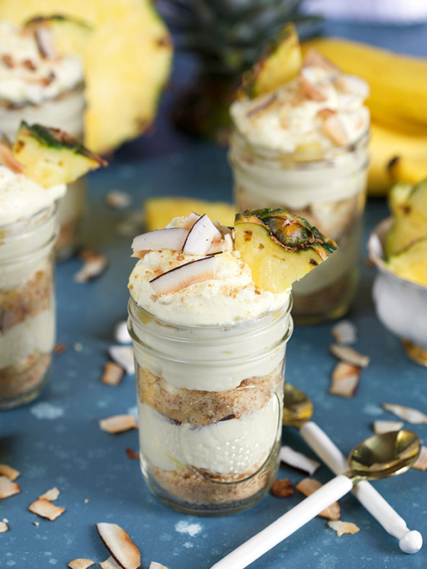 Pina colada Banana Pudding layered in jars with white spoons on blue background from TheSuburbanSoapbox.com