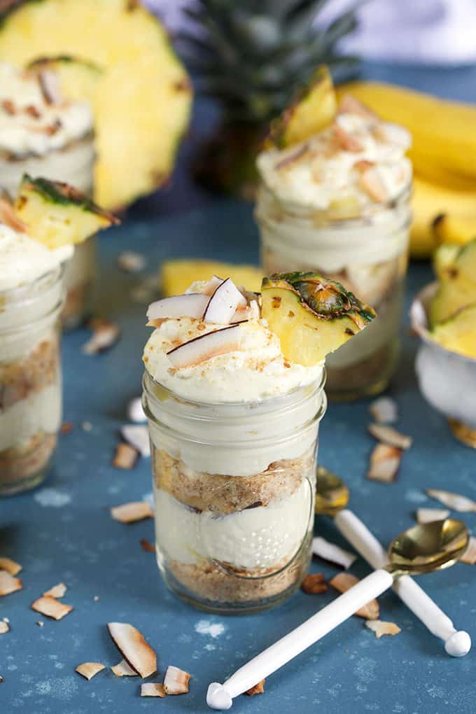 Pina colada Banana Pudding layered in jars with white spoons on blue background from TheSuburbanSoapbox.com