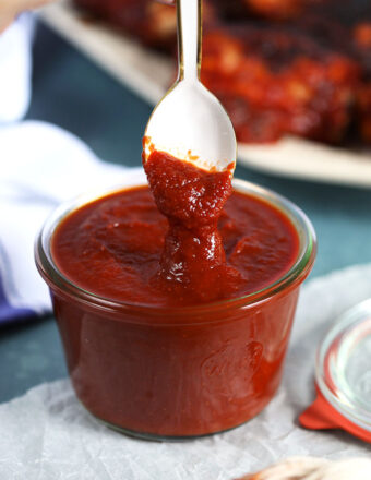 Honey Chipotle Barbecue Sauce recipe in a glass jar with a white spoon dipped into it. From TheSuburbanSoapbox.com