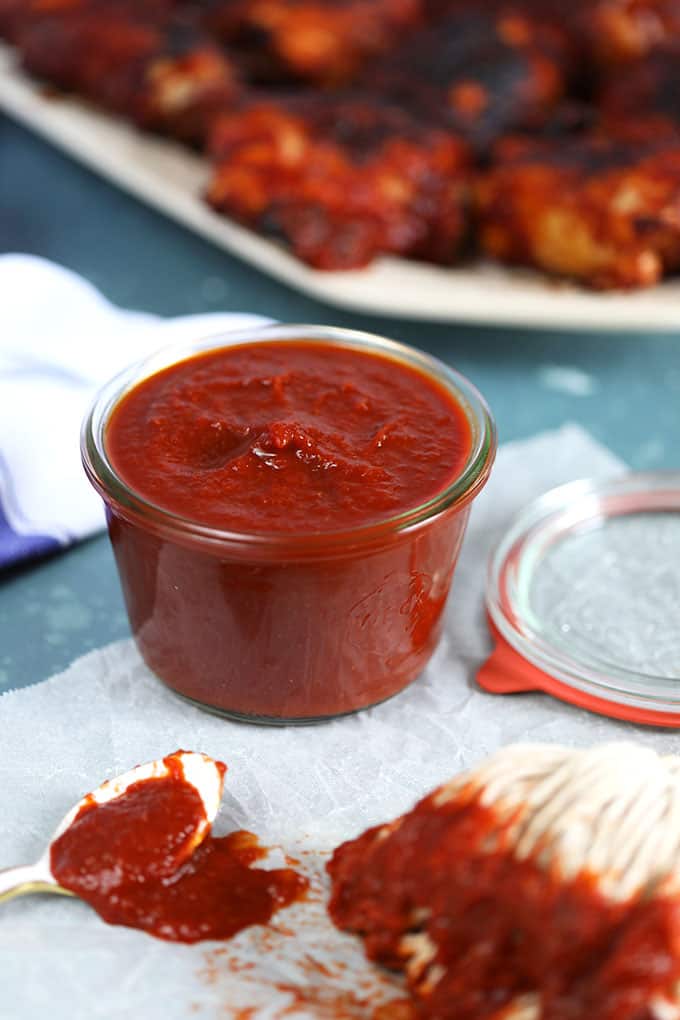 Homemade Honey Chipotle Barbecue Sauce in a glass jar with a white spoon and barbecue mop on a blue background from TheSuburbanSoapbox.com