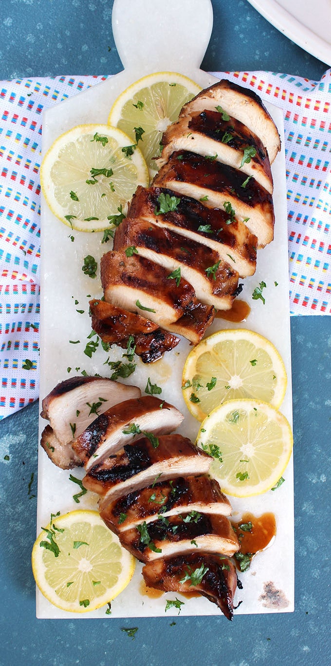 Grilled Marinated Chicken Breasts on a white platter with a blue background.