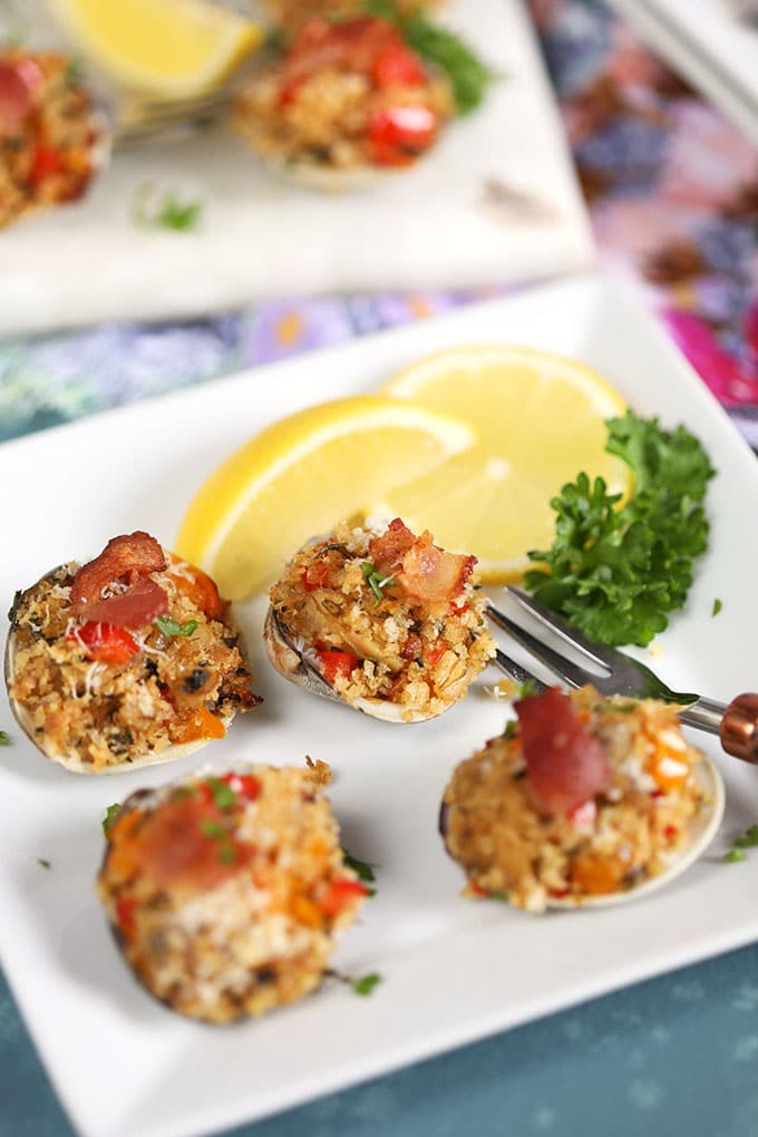 Baked Clams Casino on a white plate with lemons and parsley from ThesuburbanSoapbox.com