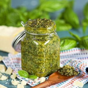 Basil pesto in a glass jar with basil in the background and wooden spoon from TheSuburbanSoapbox.com