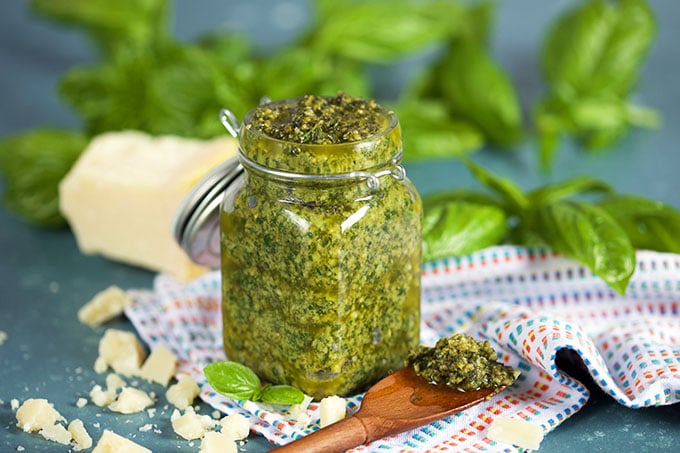 Basil pesto in a glass jar with basil in the background and wooden spoon from TheSuburbanSoapbox.com
